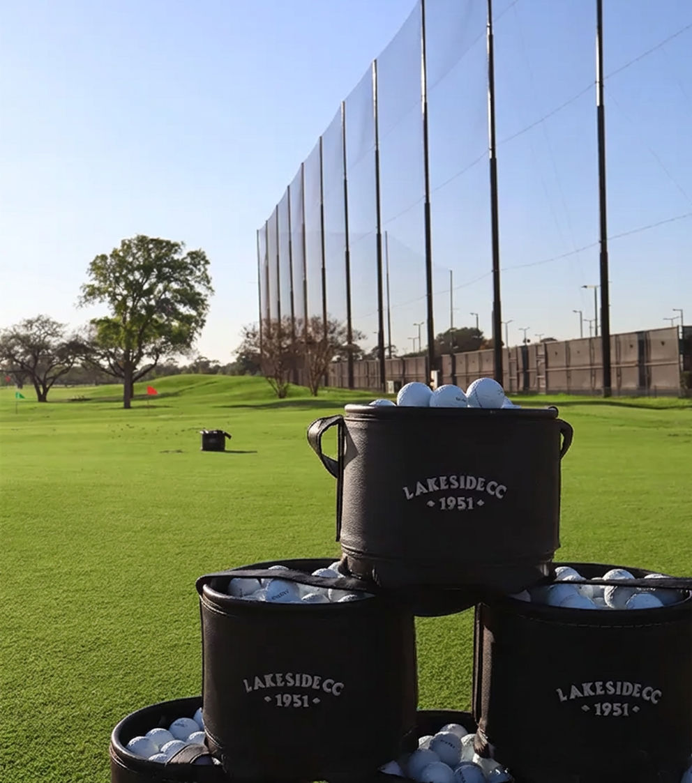 Golf balls at a driving range with high perimeter safety netting installed along the course boundary.
